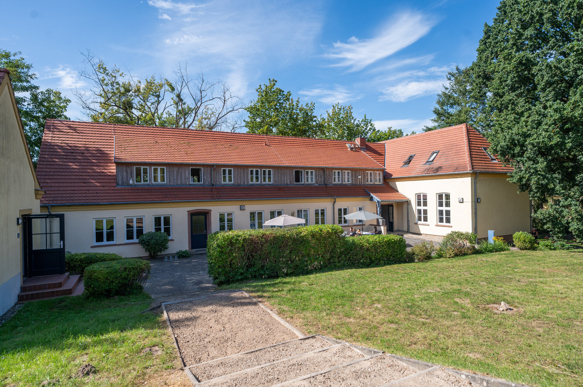Das Hauptgebäude der Bildungsstätte. Ein gelbes Haus mit rotem Dach.