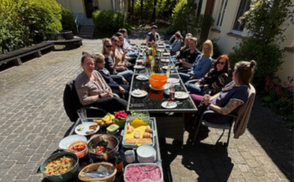 Eine Gruppe von Menschen, die draußen in der Sonnean einem gedeckten Tisch sitzen.